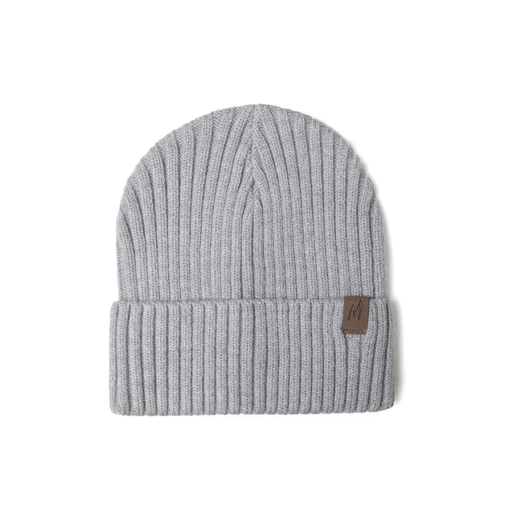 Close-up front view of navy blue ribbed knit beanie on white background showing detailed rib texture and brown leather-look tab with M logo