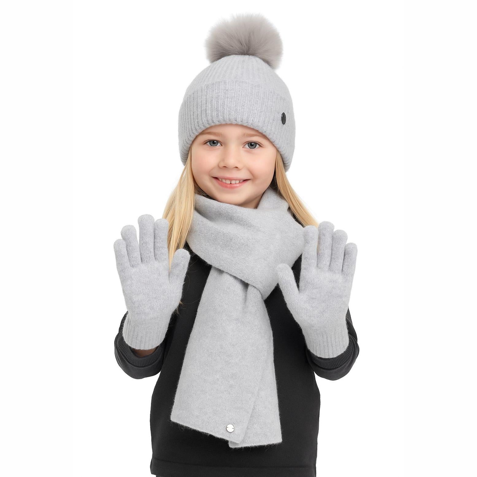 Young blonde girl wearing grey ribbed knit winter set with pompom hat, scarf and gloves, smiling against white background