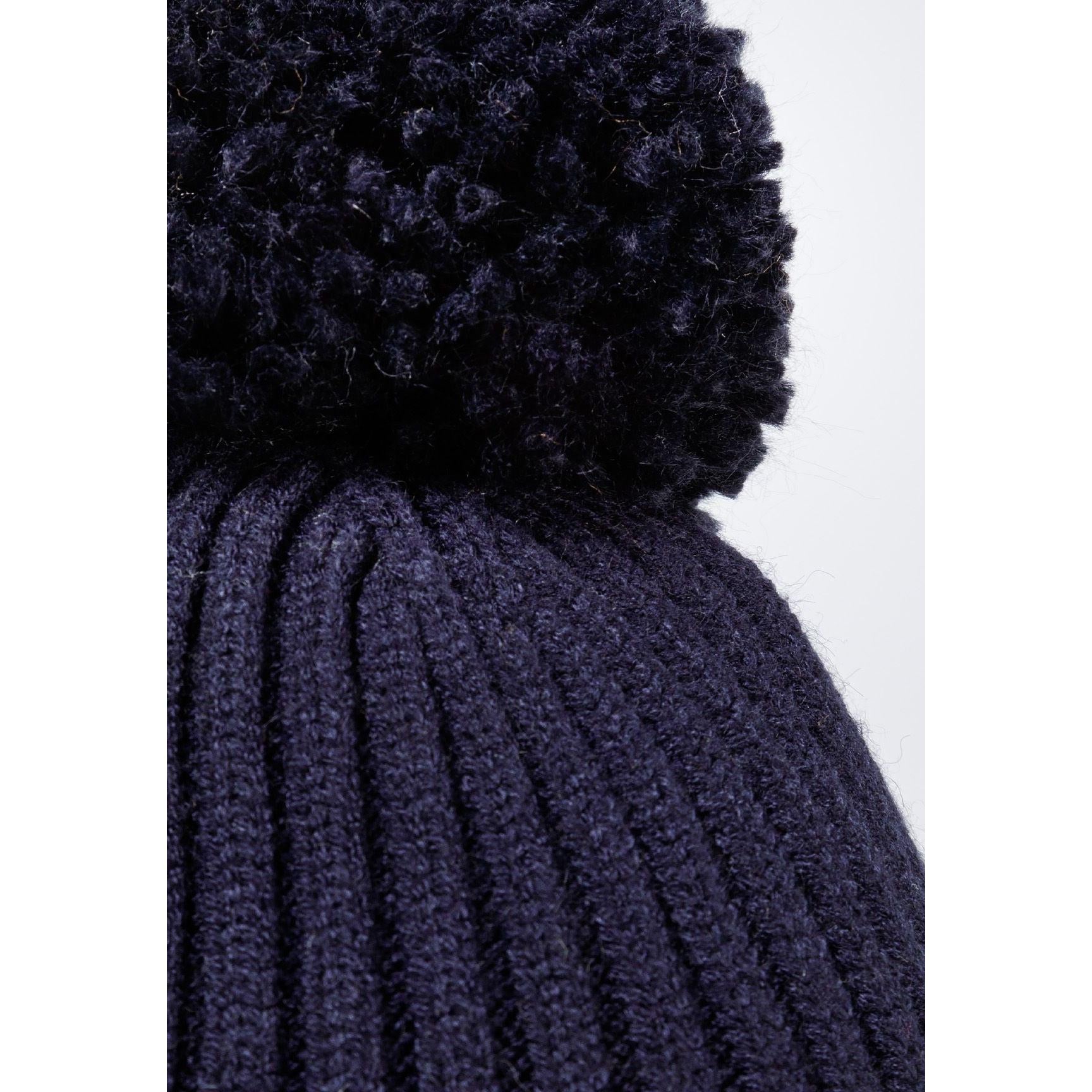 Close-up detail of navy beanie showing ribbed knit texture and fluffy black pom pom