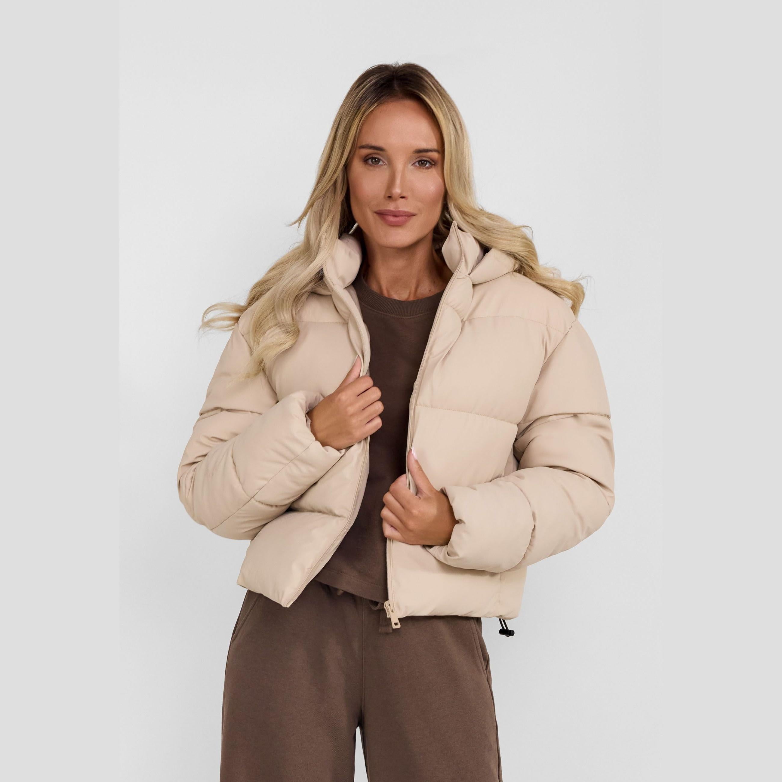 Young woman wearing stone grey quilted puffer jacket with hood over brown outfit, front view against white background