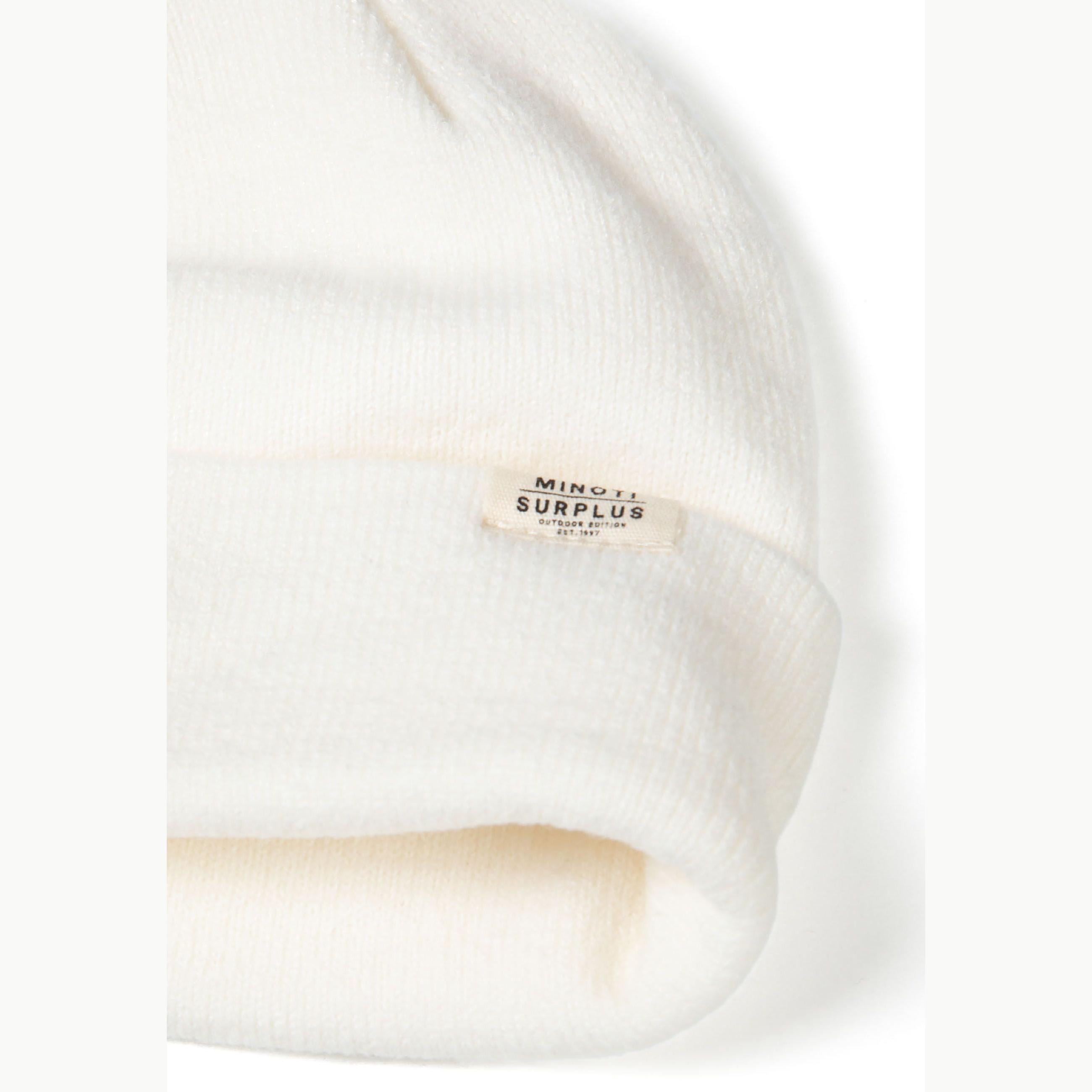 Close-up detail of cream ribbed beanie showing Minoti Surplus woven label and soft knit texture on white background