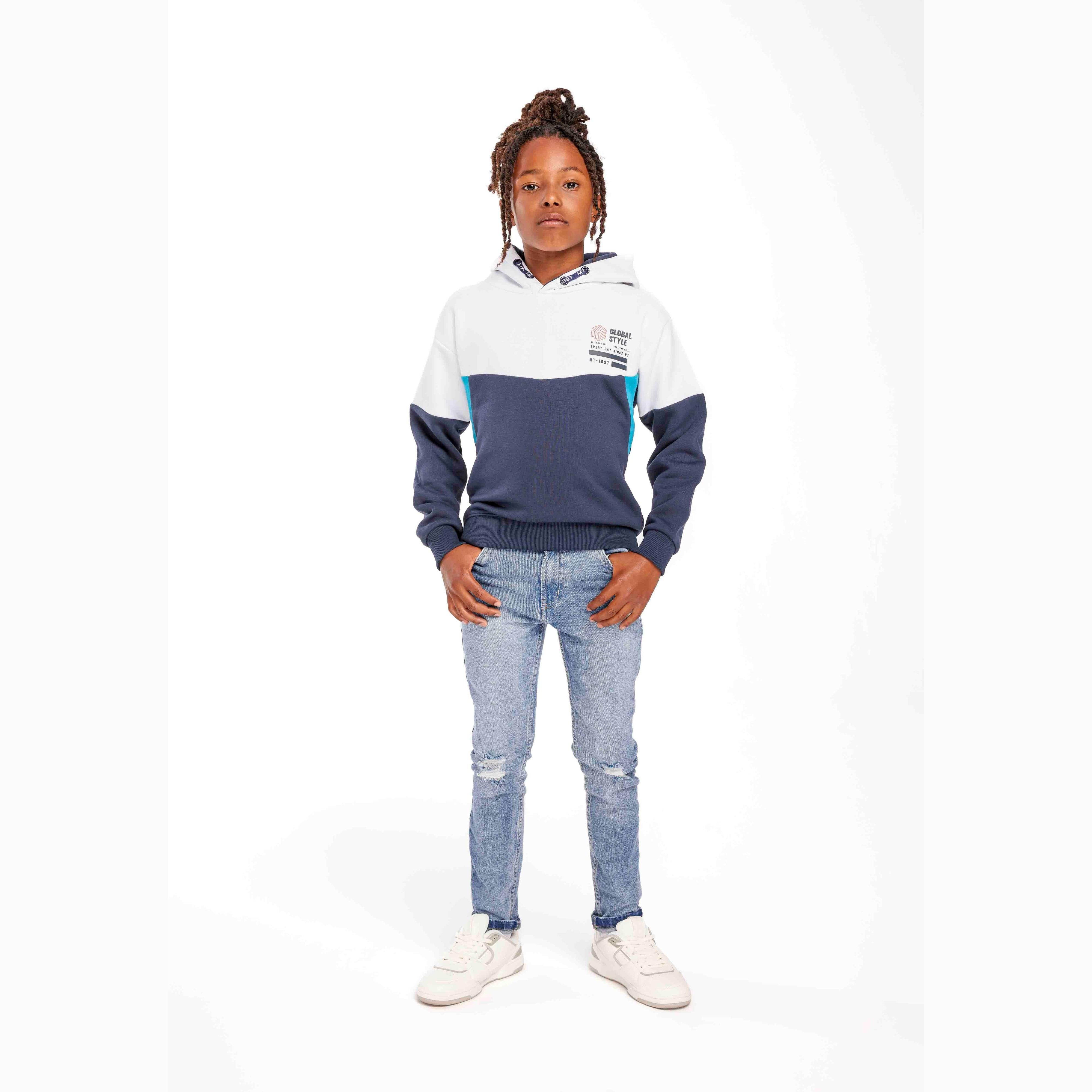 Young model wearing navy and white contrast panel hoodie with light blue jeans, hands in pockets, standing against white background