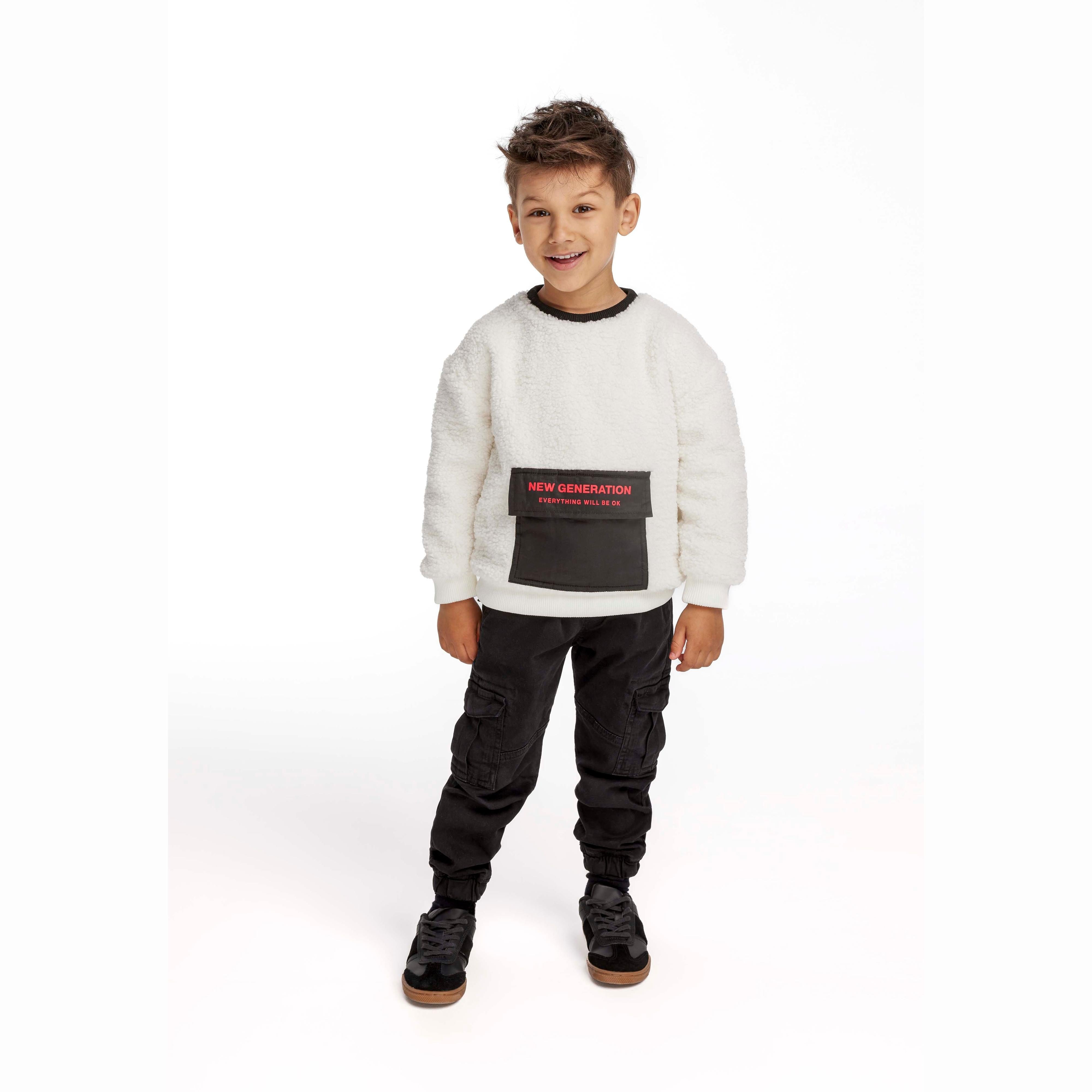 Young boy wearing cream borg sweatshirt with black contrast pocket, paired with black cargo trousers and sneakers, full body studio shot on white background