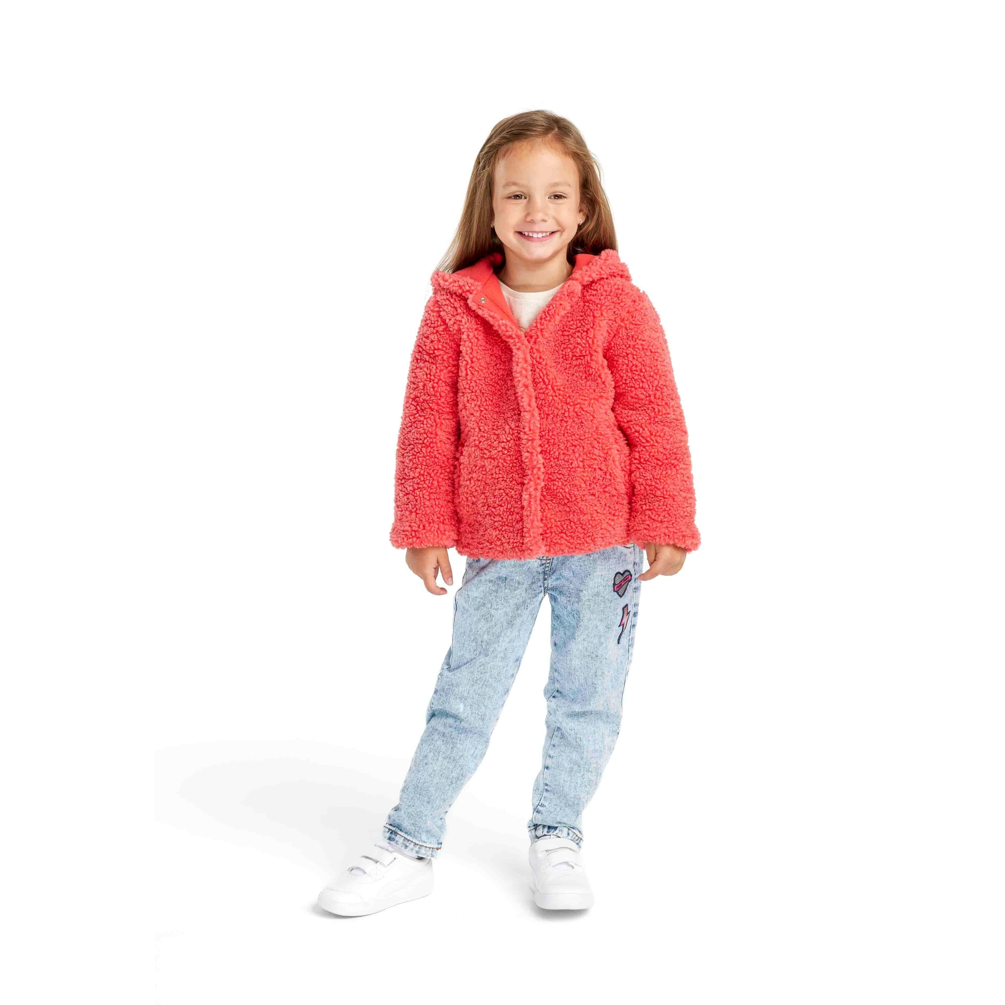 Young girl wearing coral borg fleece hooded jacket with blue jeans and white trainers, standing against white background, front view