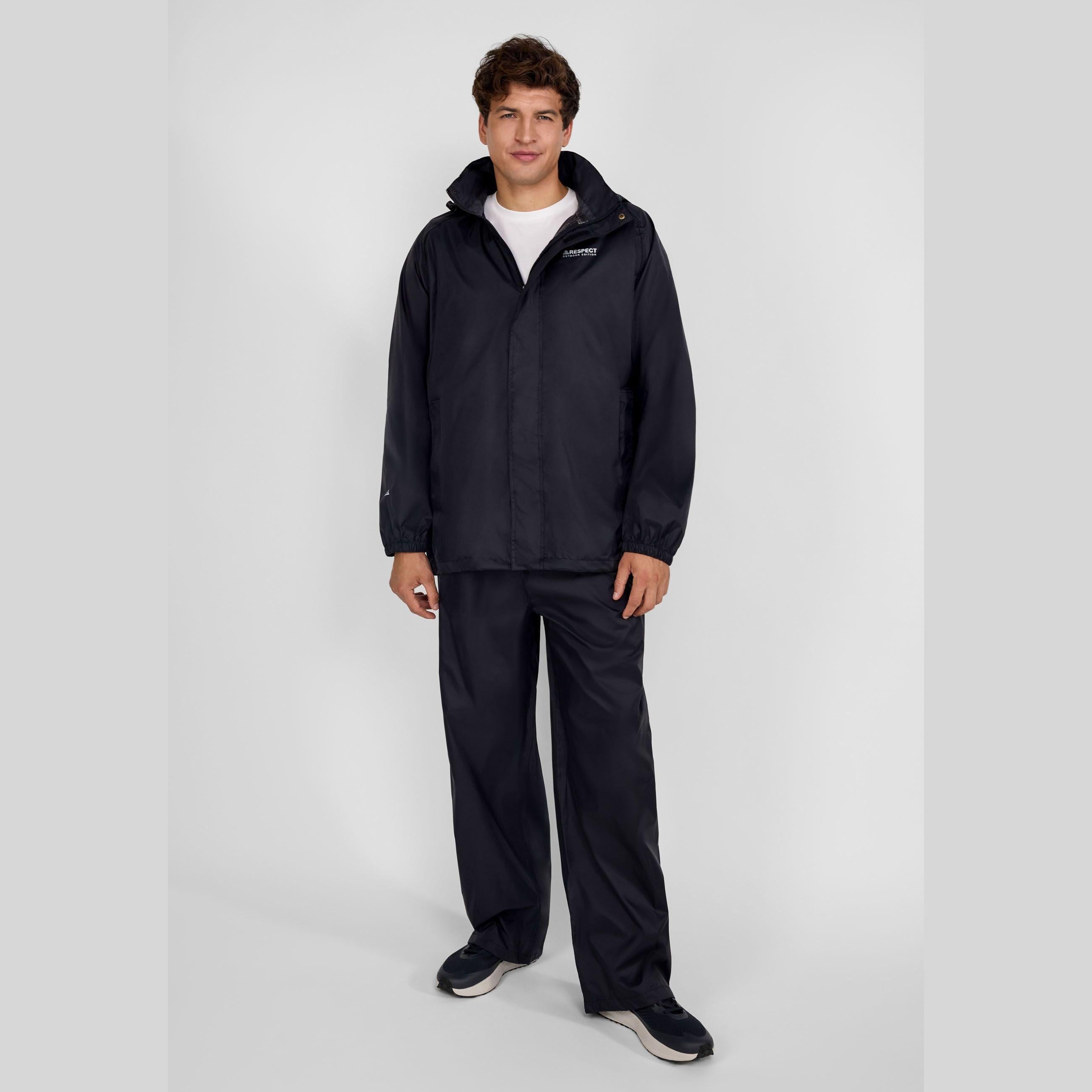 Young male model wearing complete black waterproof rain suit with jacket and overpants, standing against light grey studio background