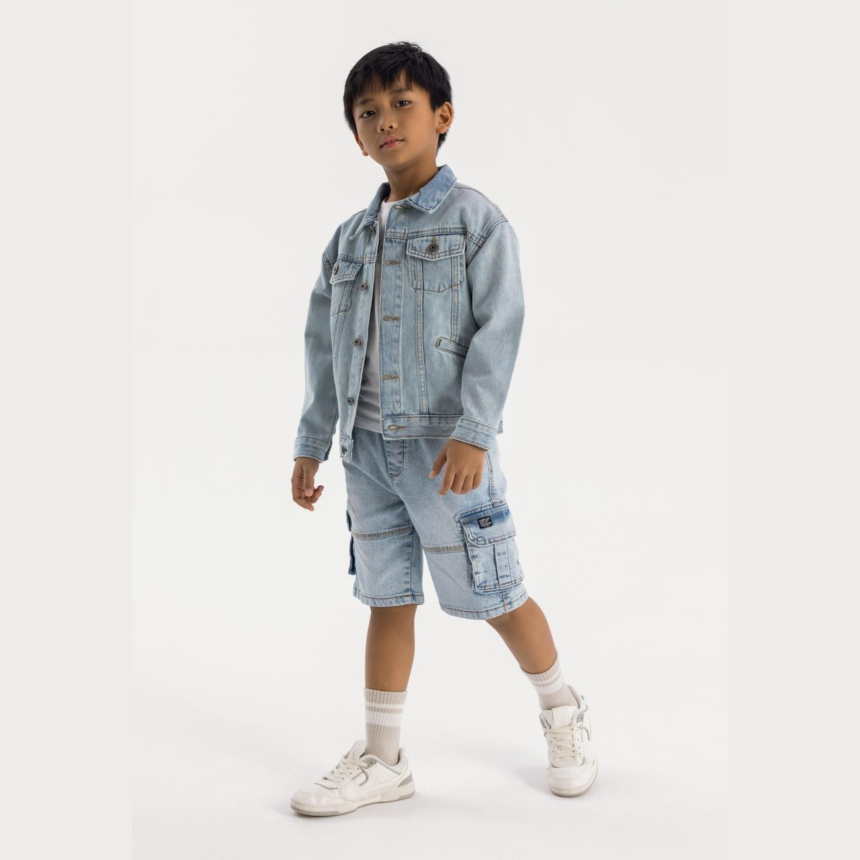 Boy wearing light blue denim cargo shorts with matching jacket, white sneakers and socks on light grey background