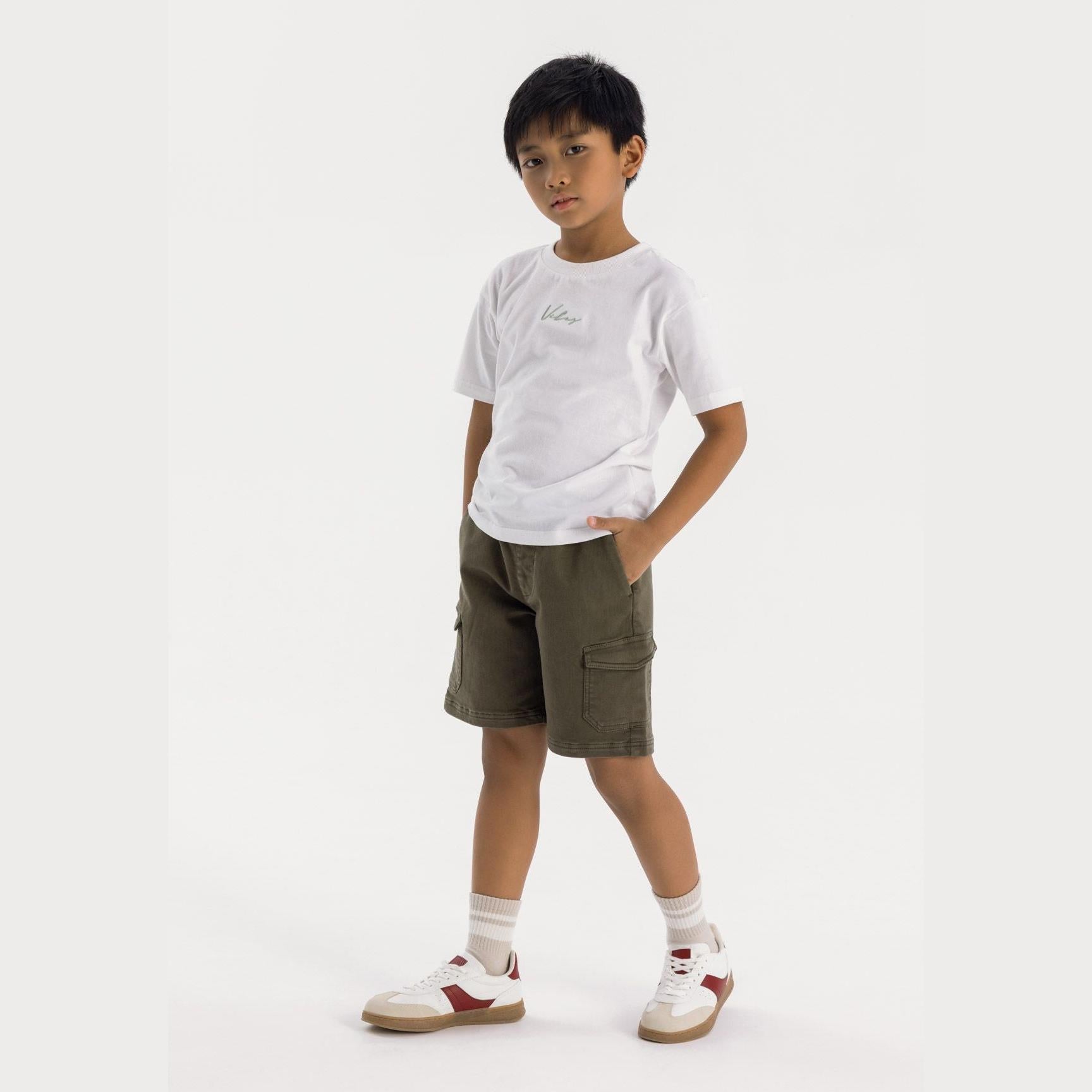 Boy wearing white t-shirt and khaki knitted cargo shorts with drawstring waist, standing against white background