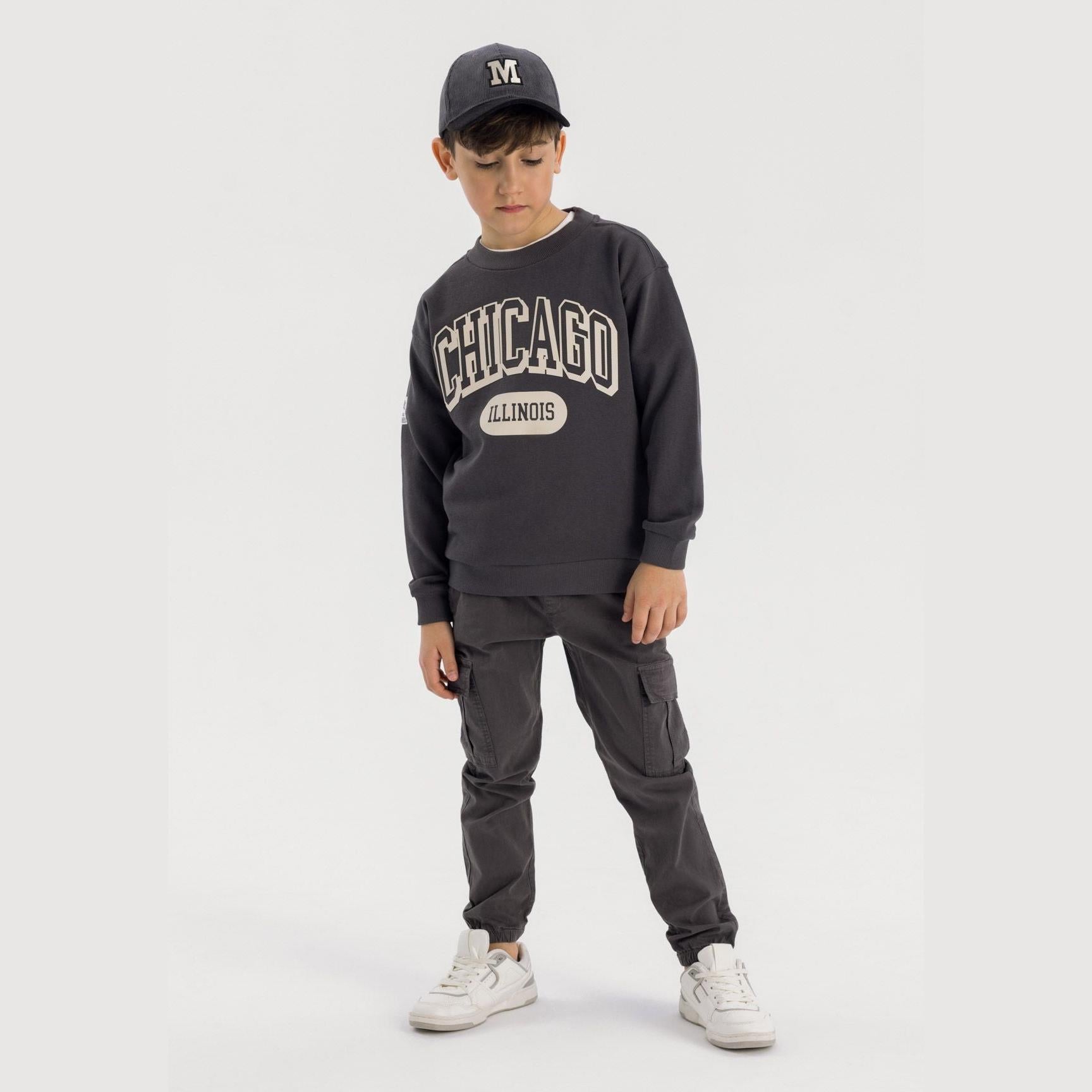 Boy wearing grey cargo trousers with Chicago sweatshirt and cap, full body front view on white background
