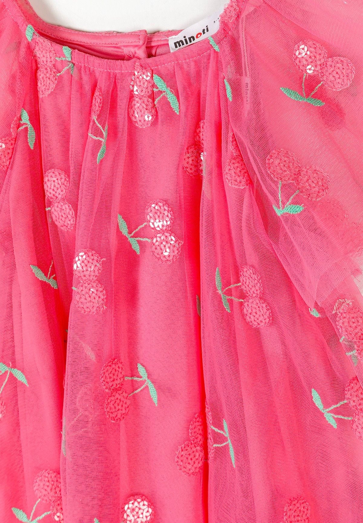Close-up detail of pink tulle fabric showing sequin cherry pattern with green leaves and Minoti brand label at neckline