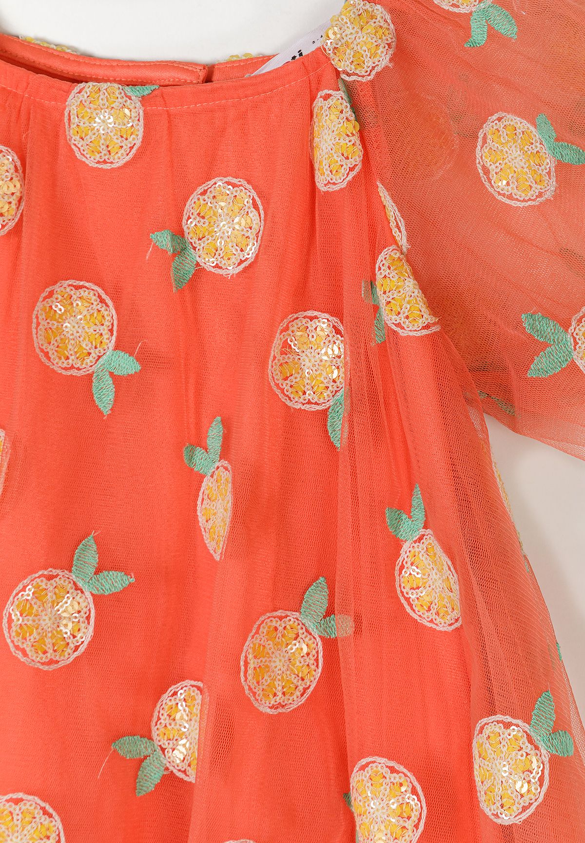 Close-up detail of orange tulle fabric showing yellow sequin citrus embellishments and green leaf details with button closure visible