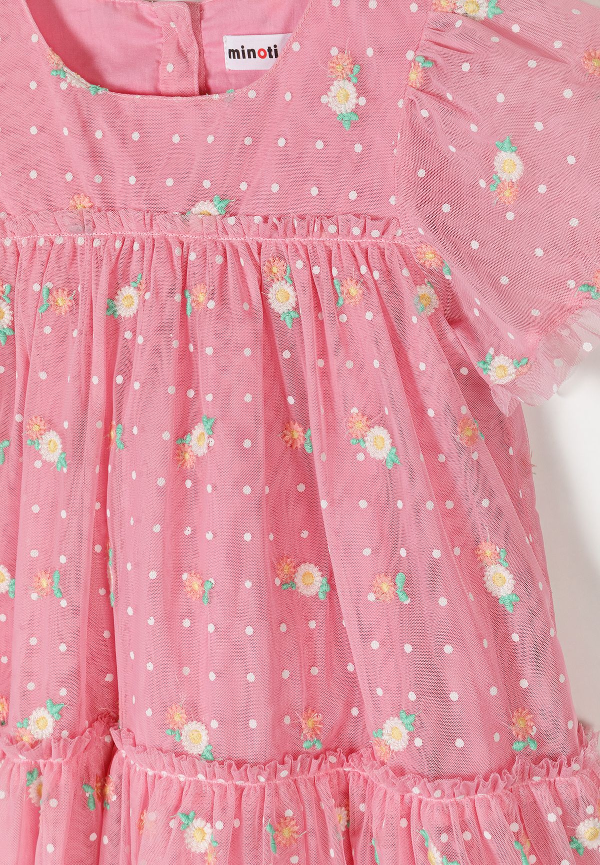 Close-up detail of pink tulle fabric showing white polka dots, floral embroidery and Minoti brand label at neckline