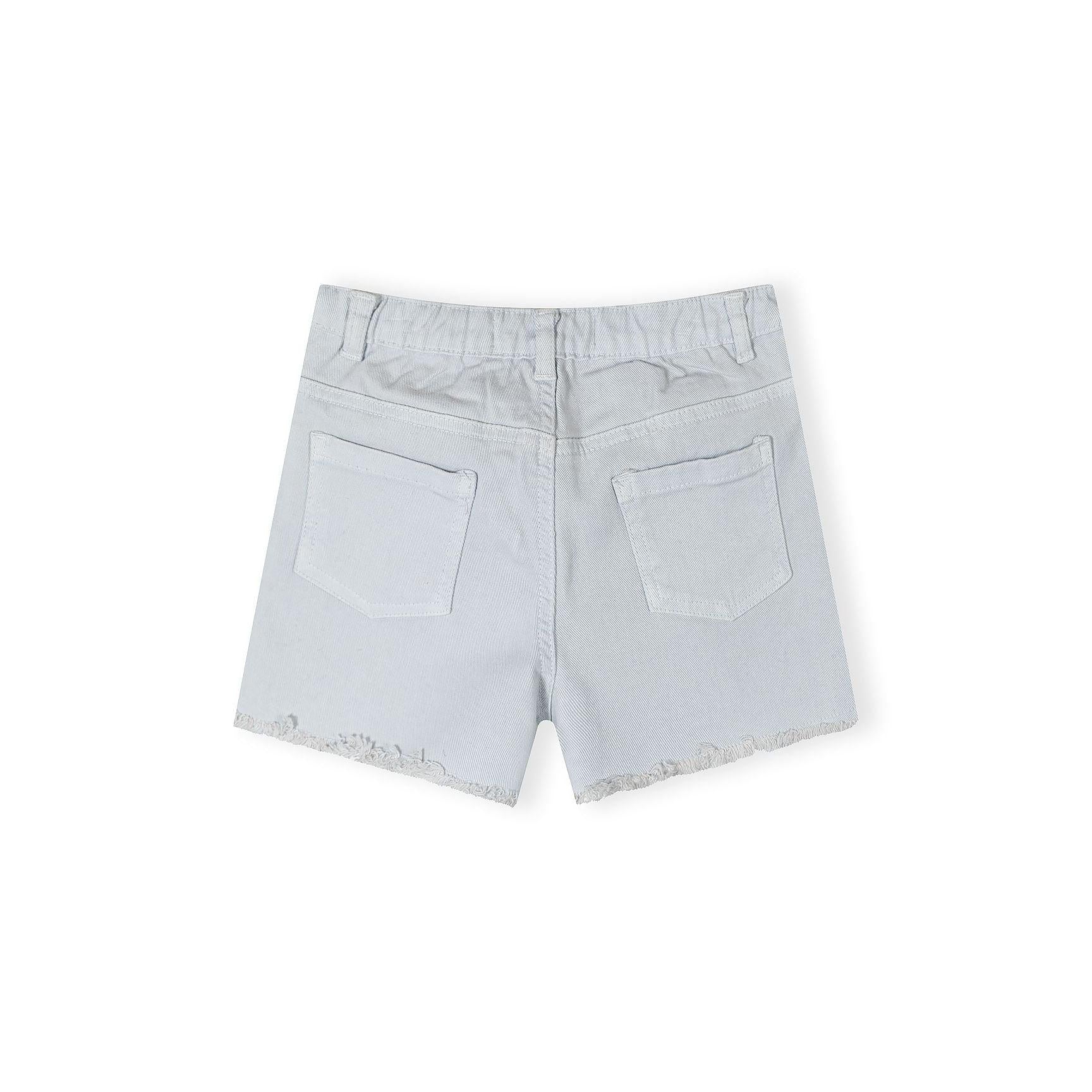 Close-up detail of white twill shorts showing Minoti brand label in waistband reading '6-7 YRS 110/116 CM MADE IN PAKISTAN' with button closure visible