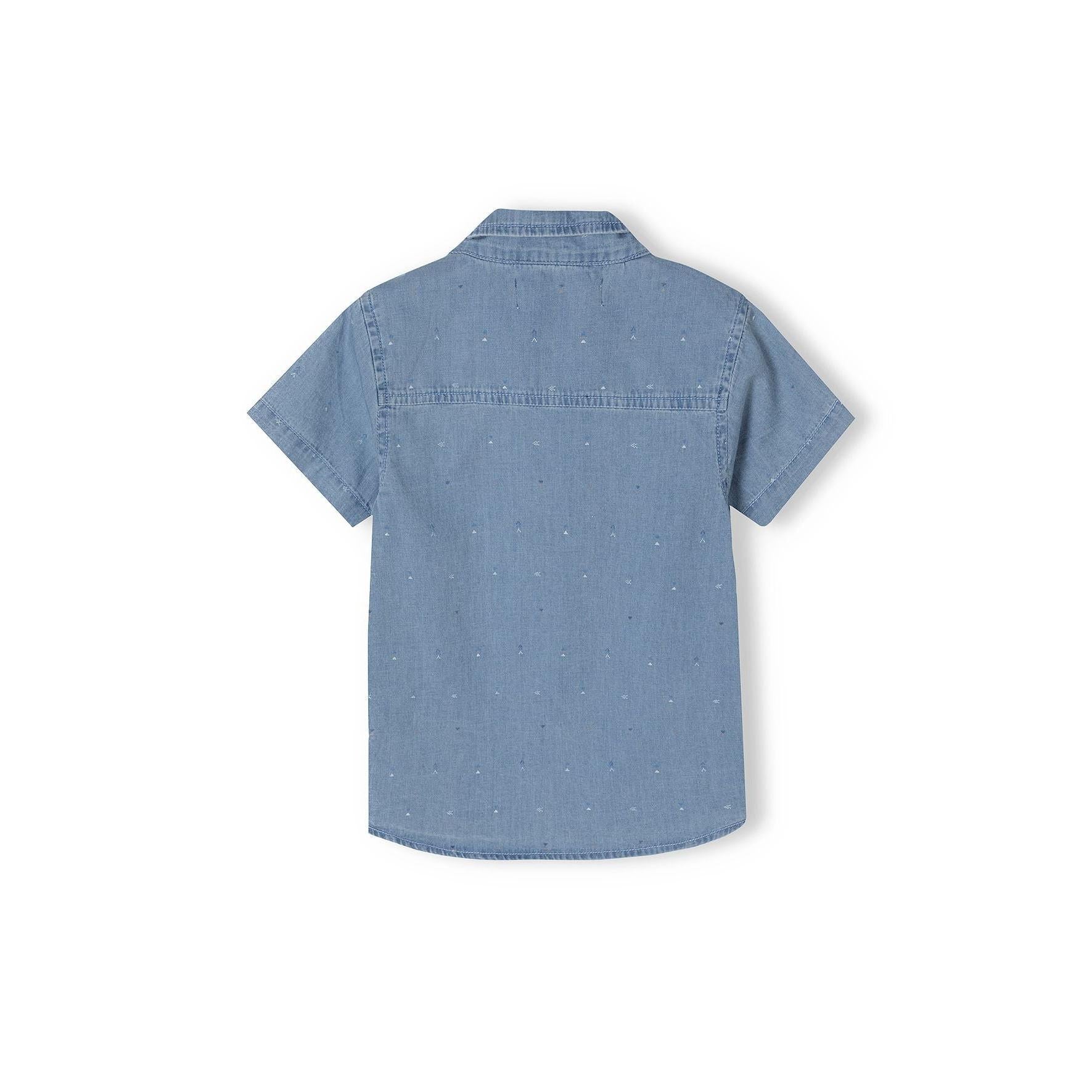 Close-up detail of light blue denim shirt showing brown buttons, chest pocket and speckled print pattern