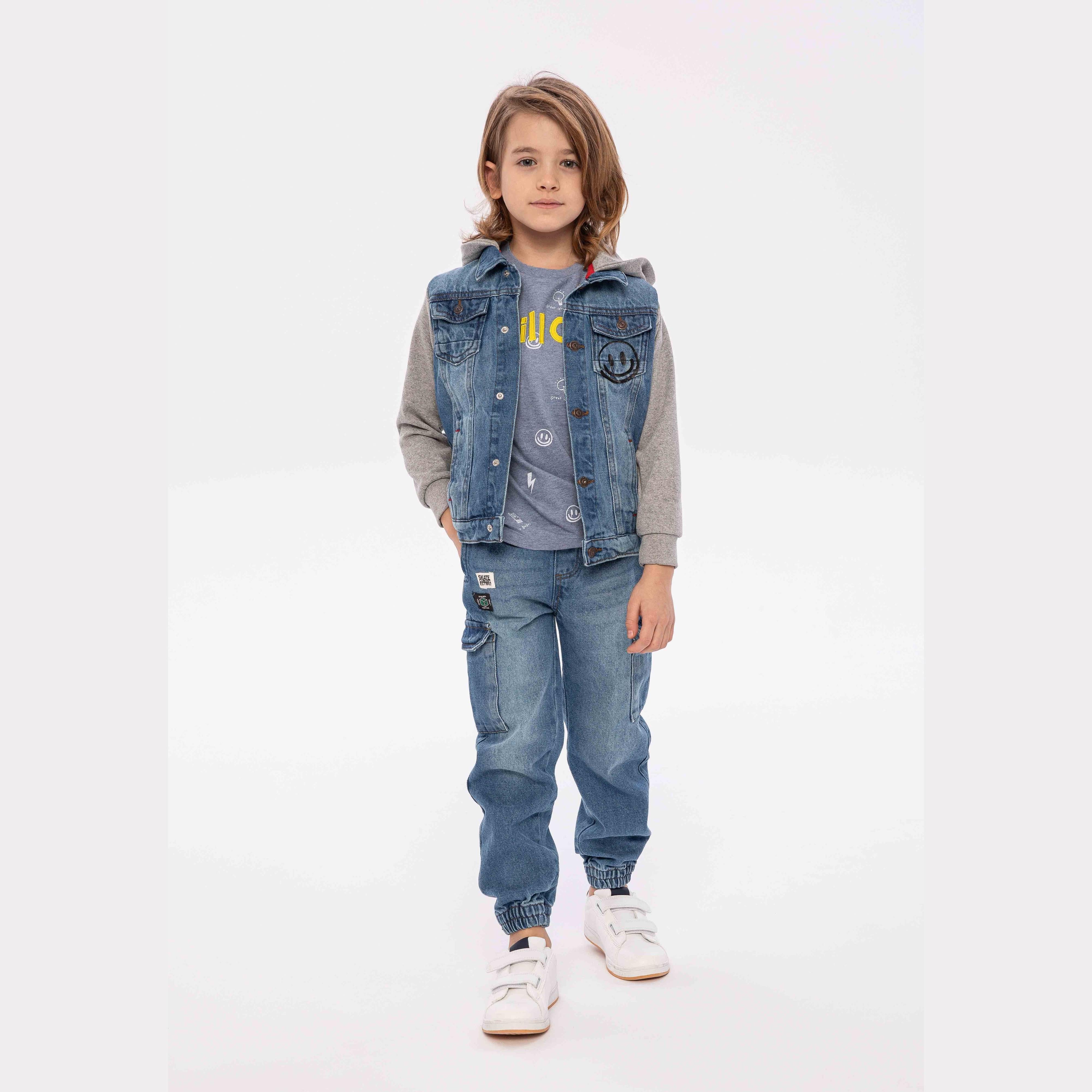 Young child wearing light blue denim jacket with grey fleece hood and sleeves, paired with matching denim joggers and white trainers, standing against white background