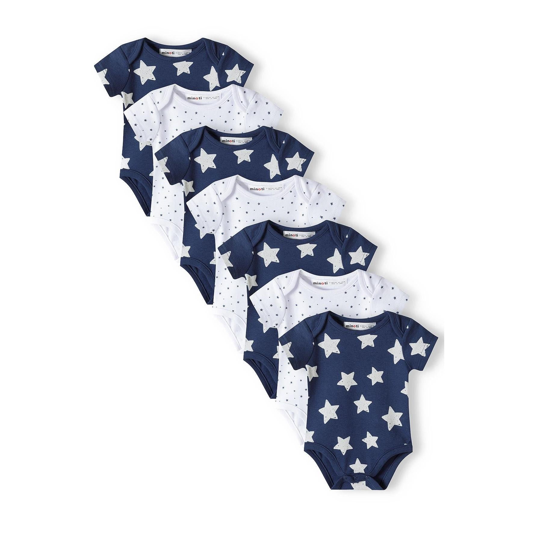 Seven baby bodysuits arranged in diagonal line showing alternating navy with white stars and white with navy micro star patterns on white background