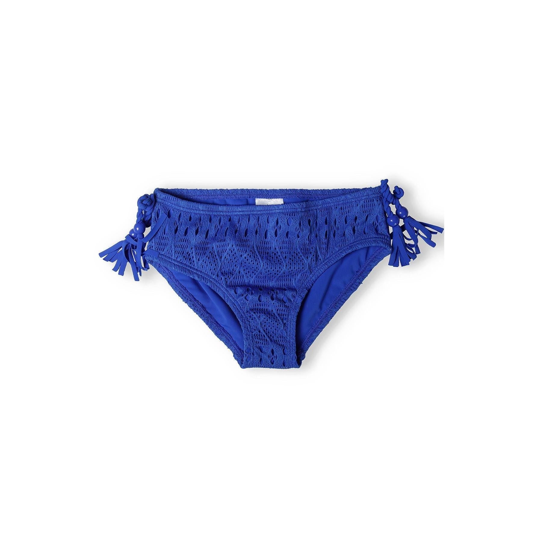 Close-up view of cobalt crochet bikini bottoms showing decorative side tassels and intricate textured fabric pattern on white background