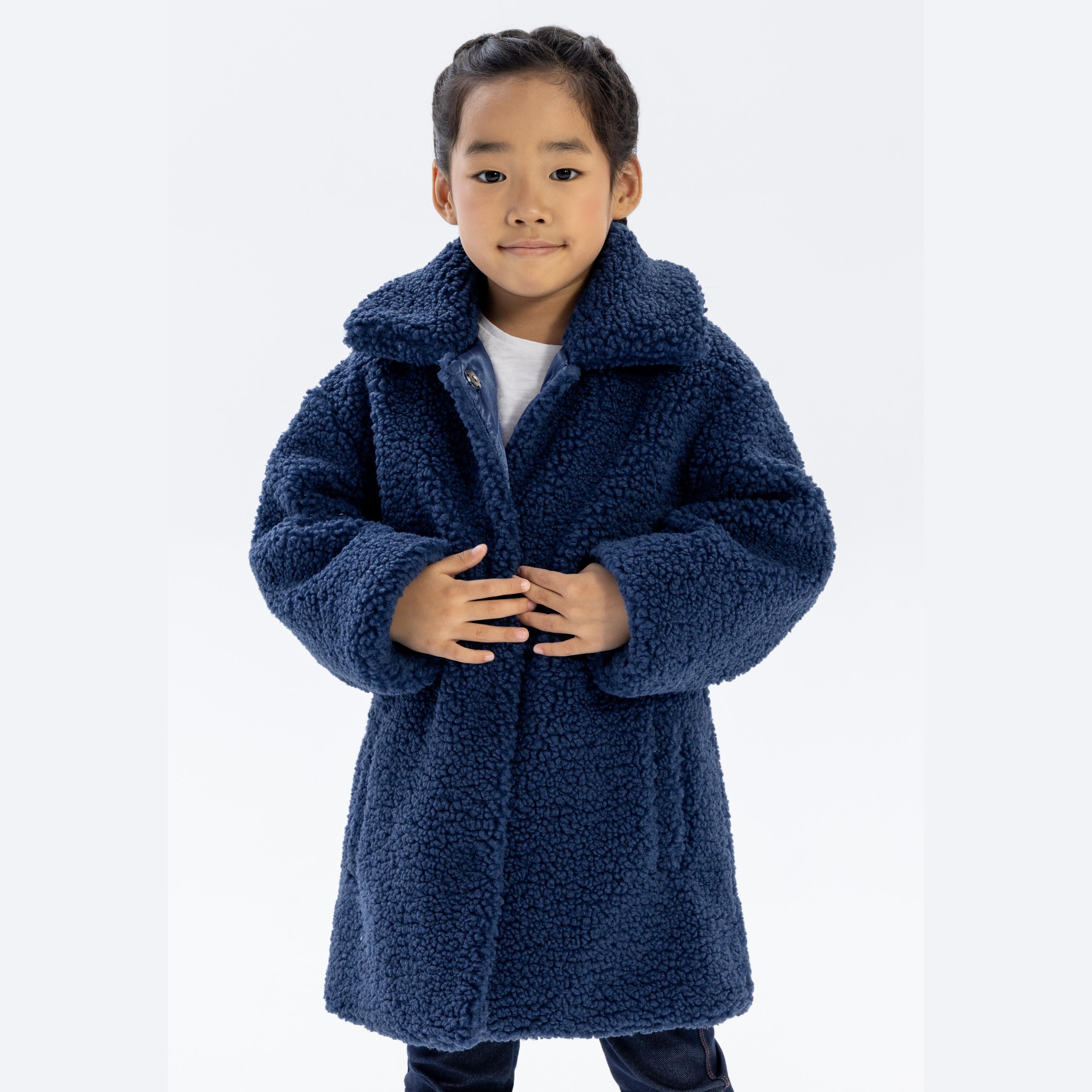 Young Asian girl wearing navy blue boucle coat with sherpa collar, hands clasped together, smiling on white background