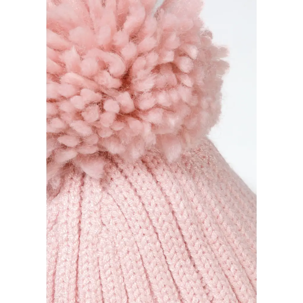 Detail shot of pink beanie showing fluffy dusty pink pom pom and ribbed knit texture with ear flap construction