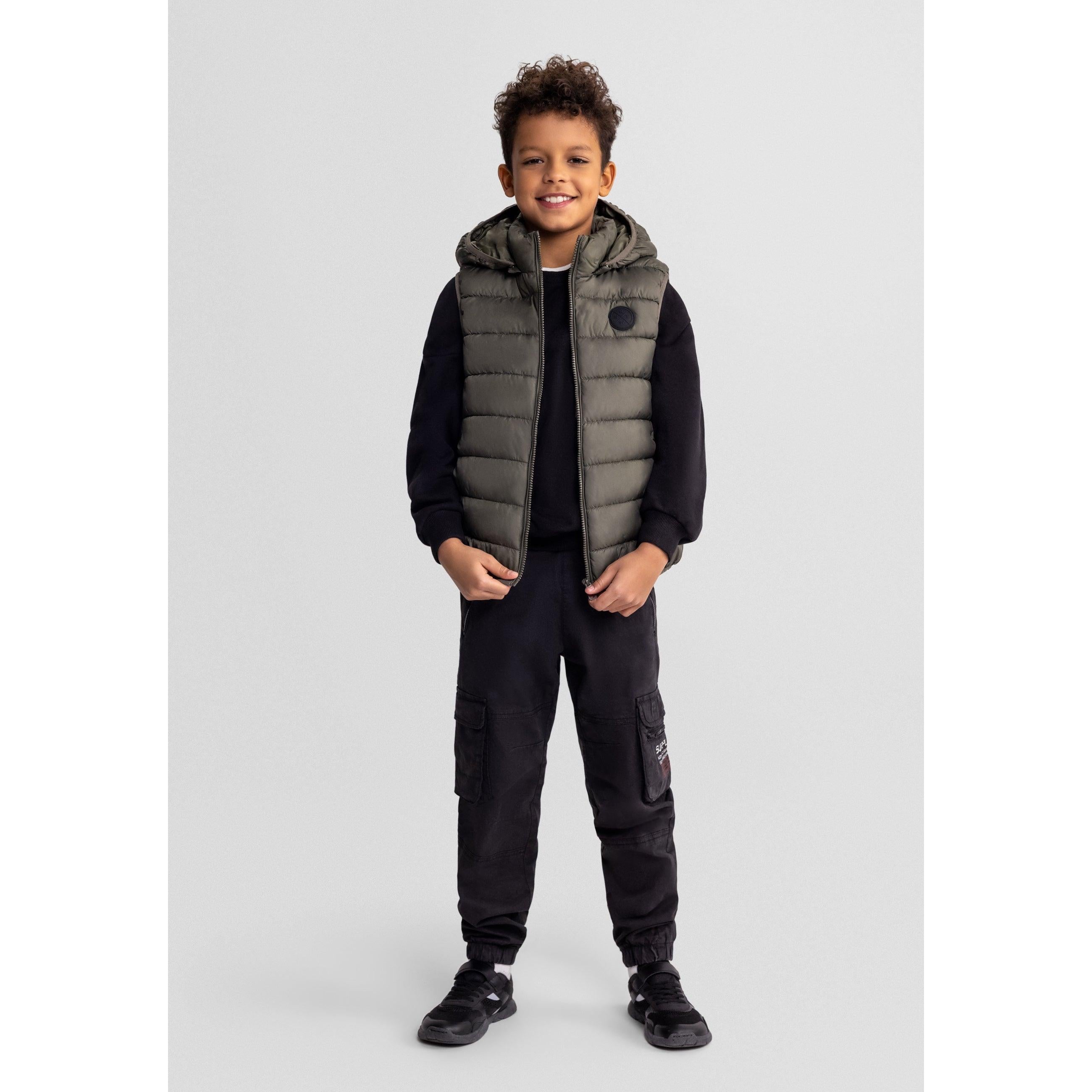 Boy wearing khaki padded gilet with black joggers and black trainers on light grey background