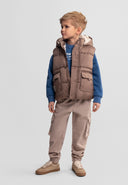 Young boy wearing a beige hooded gilet with teddy fleece lining and patch pockets in stylish kids fashion design