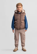 Young boy wearing a beige hooded gilet with teddy fleece lining and patch pockets in a stylish kids fashion design.