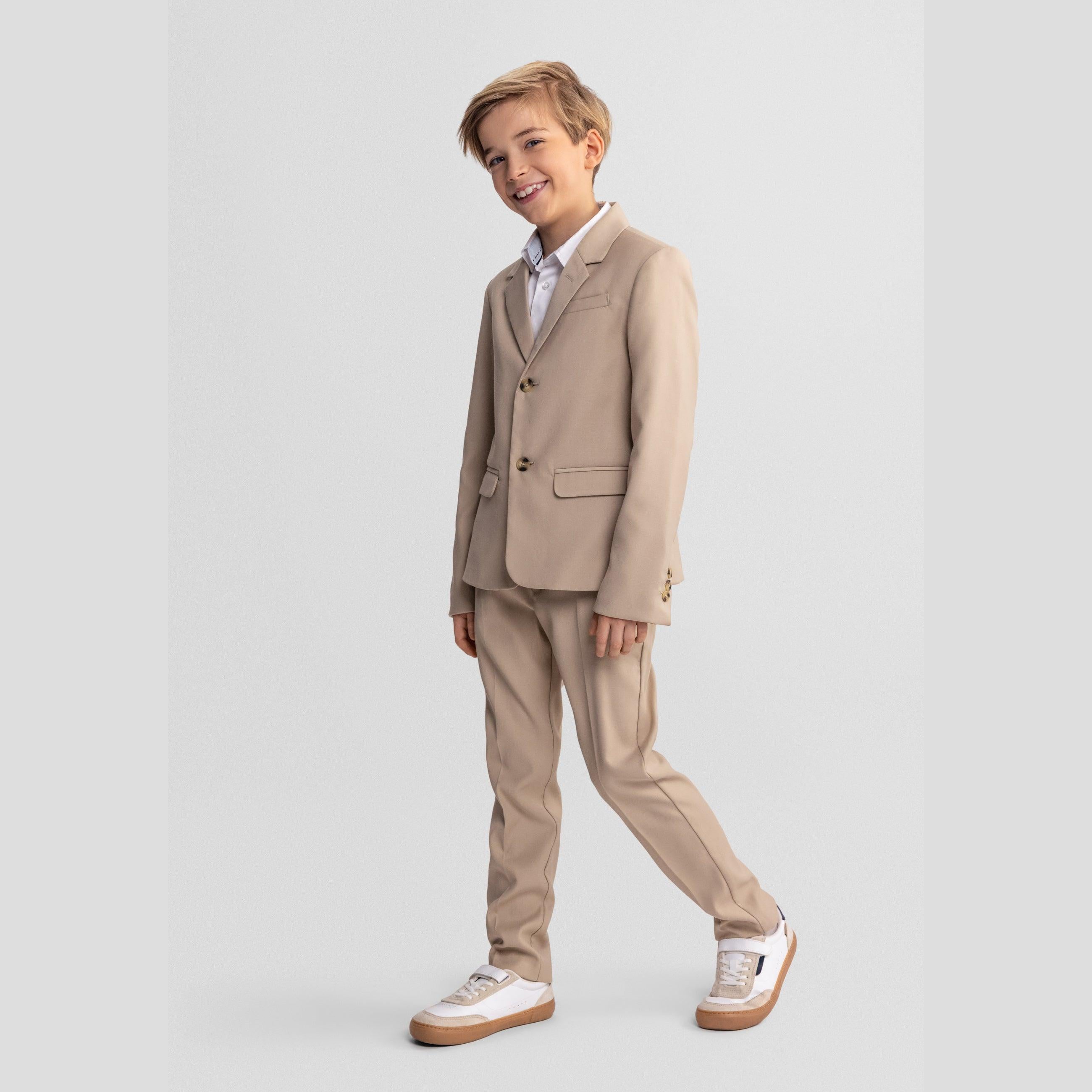 Full length view of boy in complete stone suit pointing at camera, wearing white trainers against grey studio background