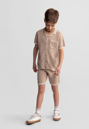 Young boy wearing beige knitted cotton polo shirt and shorts set with a unique textured design and white trim details