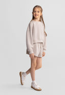Young girl wearing a beige sweatshirt and shorts set with elasticated waist, showcasing a modern kids fashion design