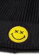 Close-up of a black knitted beanie with a yellow smiley badge.