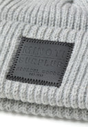 Detail of a grey knitted hat with a black logo badge.