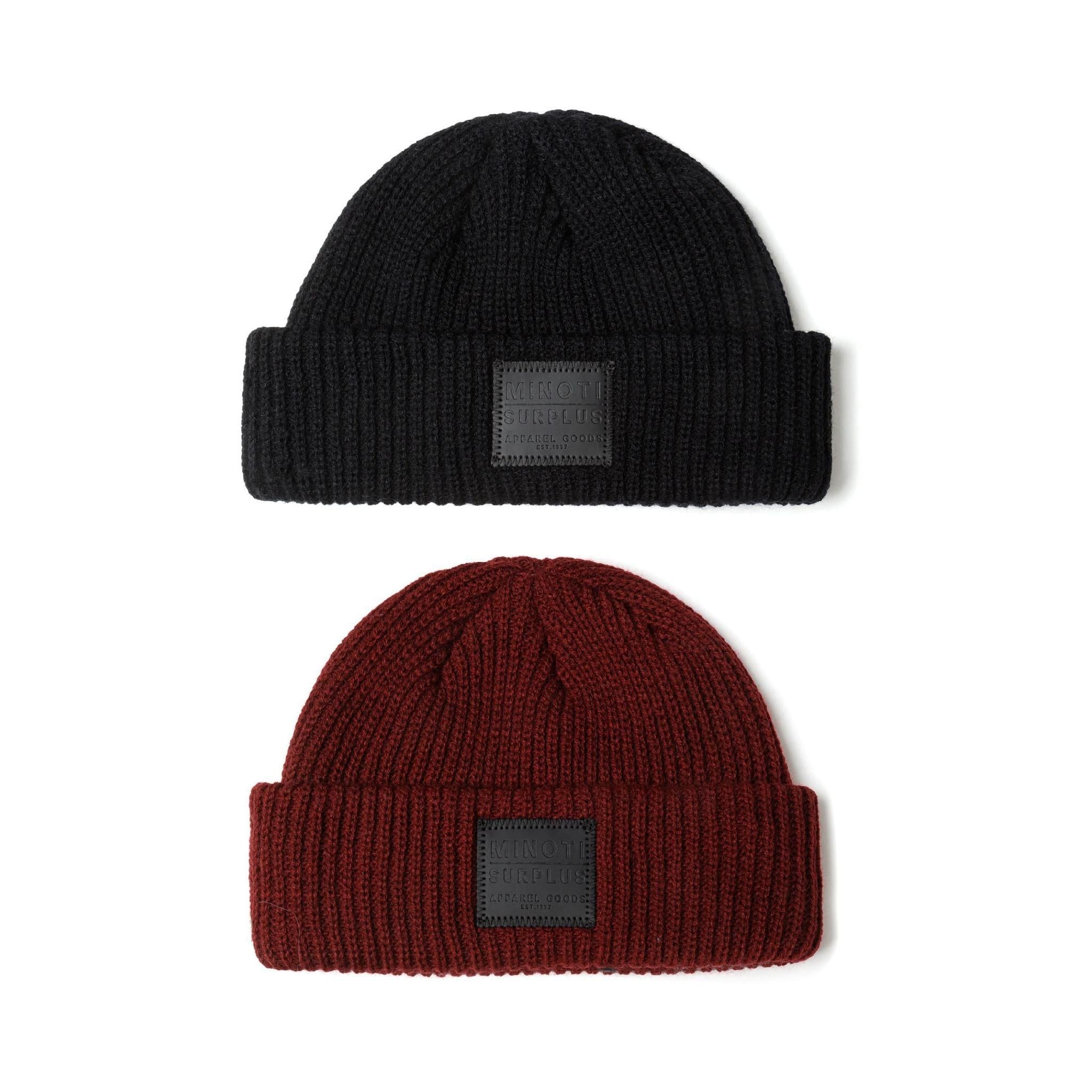 Two ribbed knit fisherman beanies displayed on white background, one black and one burgundy, both featuring dark grey Minoti Surplus rectangular patch labels
