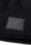 Detail of a black knitted fisherman hat with a front badge.