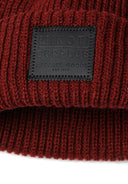 Detail of a knitted hat with ribbed edges and a black badge.