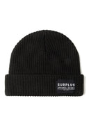 Detail of a black rib knit beanie with a logo badge on the front.