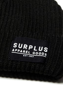 Detail of a black ribbed knit hat with a logo badge.