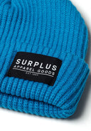 Detail of a turquoise rib knit hat with a black logo badge.