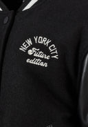 Detail of boys baseball jacket with black felt body and faux leather sleeves, featuring 'New York City' print.