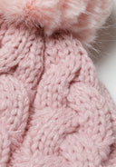 Detail of a girls' knitted cable pom pom hat in light pink with a textured cable knit pattern.