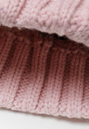 Detail of a light pink knitted cable pom pom hat with ribbed edge.