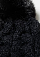 Close-up of a black knitted cable pom pom hat with a textured pattern.