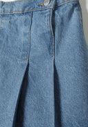 Detail of girls denim skirt with pleats, featuring a front fastening and structured pleats.