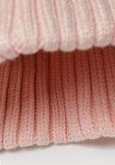 Detail of a pink ribbed baby beanie with a pom pom.