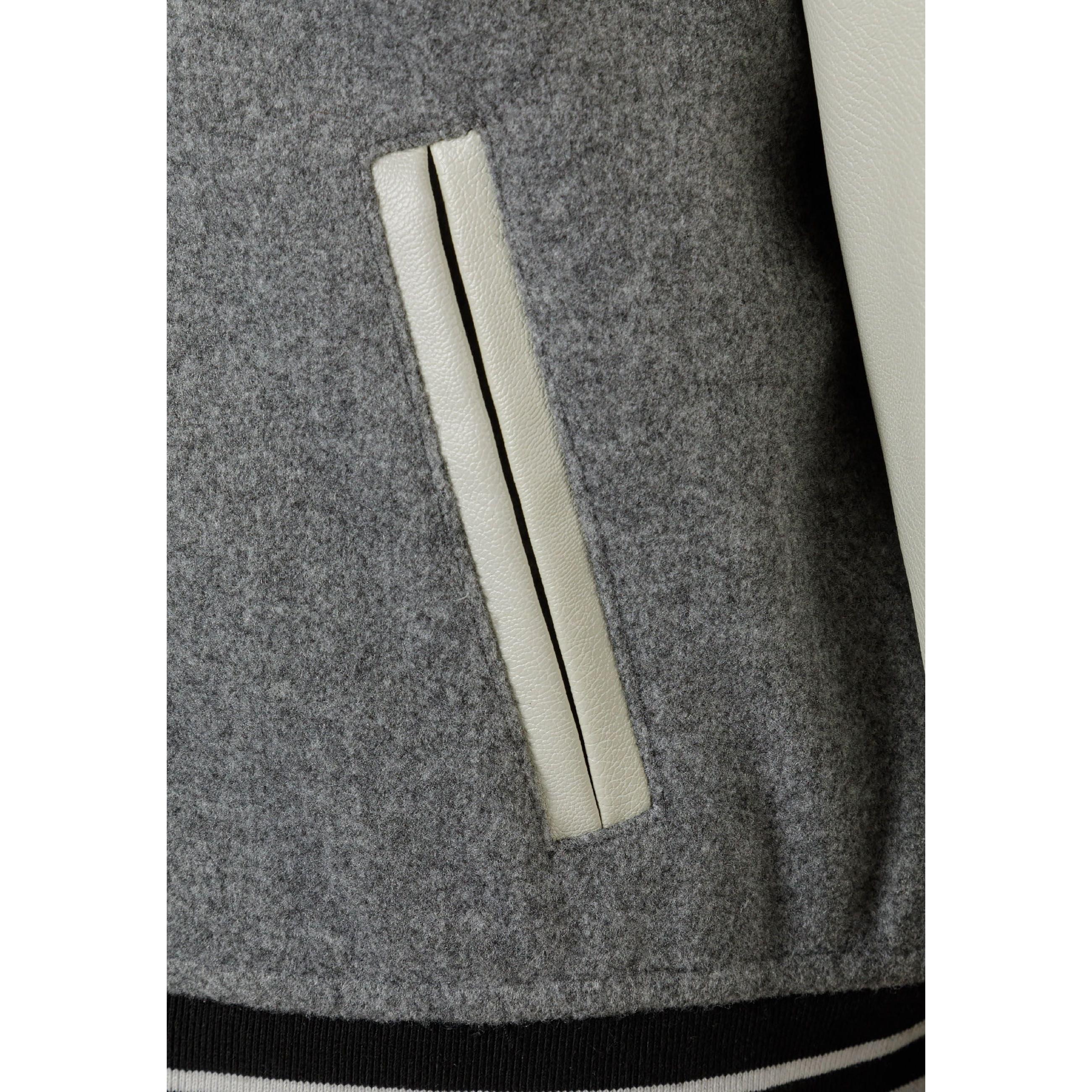 Close-up detail of cream PU sleeve pocket with piped edge on grey varsity jacket