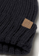 Detail of a black knitted beanie with a ribbed texture and a leather logo patch.