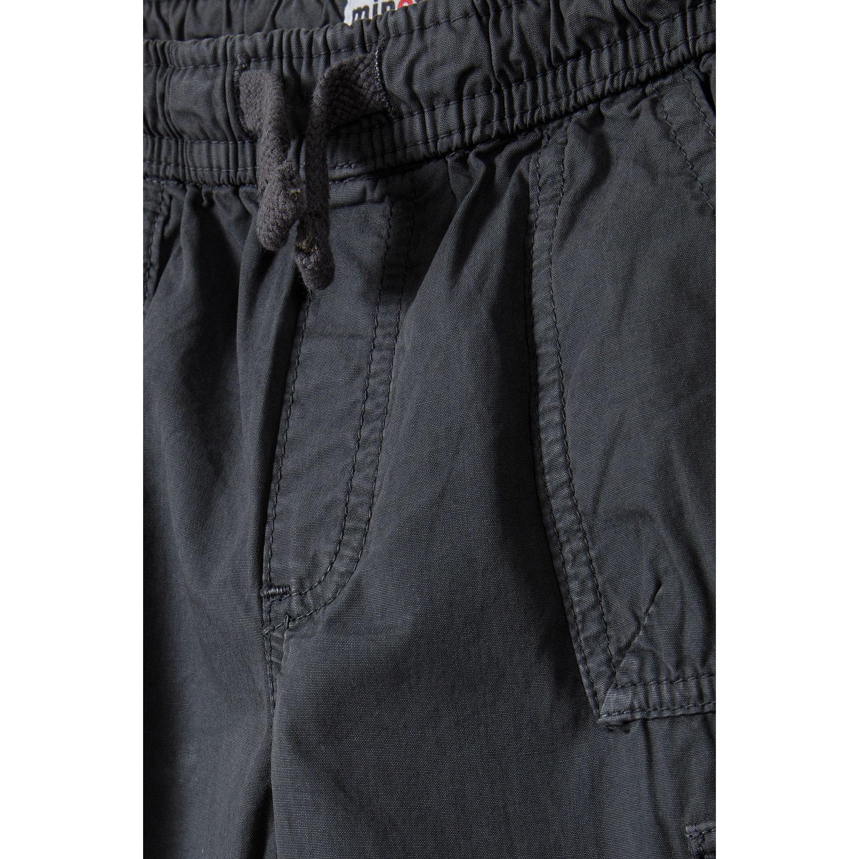 Close-up detail of black combat trouser waistband showing elasticated waist with black drawcord ties and front pocket opening