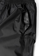 Close-up of black waterproof overpants with elasticated waistband and side pocket access.