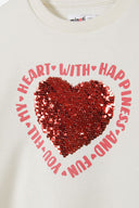 Detail of a cream girls fleece crew sweatshirt featuring a red sequin heart print.