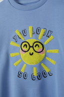 Close-up of a light blue girls fleece crew sweatshirt featuring a sun graphic with the text 'YOU LOOK SO COOL'.