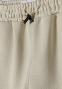 Detail of shorts with elasticated waistband and drawstrings in neutral color.