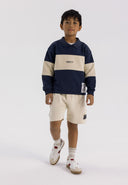 Boy wearing a navy fleece jumper with a polo collar and cream panels, paired with shorts.